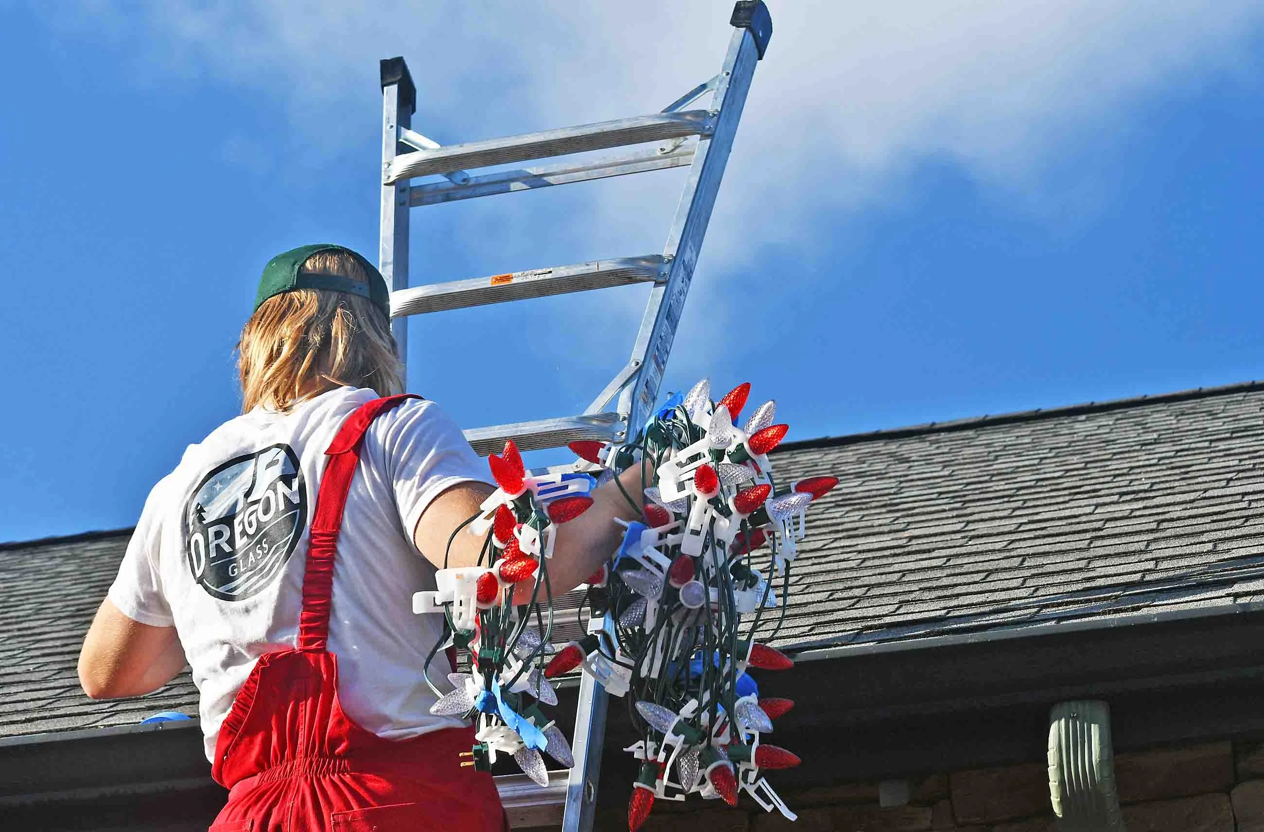 Professional Christmas light installer climbing ladder to install holiday lights on home in Eugene, Oregon